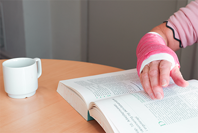 Billedet viser et håndled i gips som bladrer i en bog